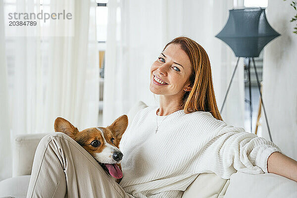 Happy woman sitting with dog in living room at home