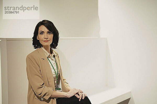 Confident mature businesswoman wearing blazer sitting on white seat at office