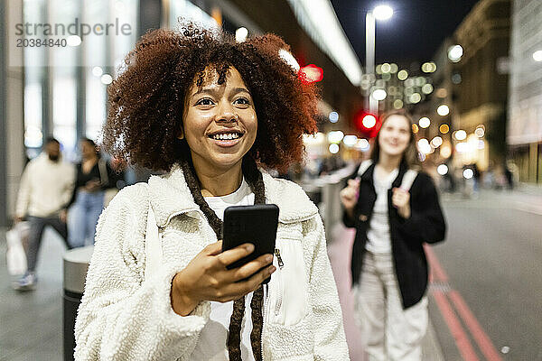 Happy woman holding smart phone and standing on street