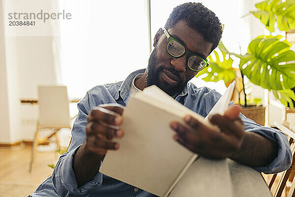 Non-binary person reading book in living room at home