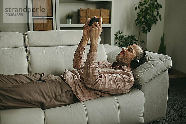 Man lying down and watching movie on smart phone at home