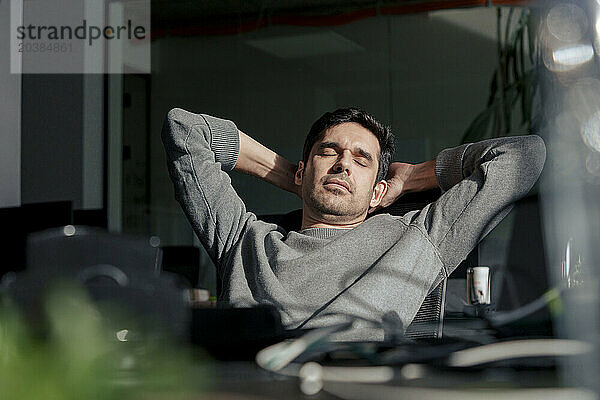 Tired businessman relaxing with hands behind head in office