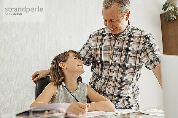 Smiling girl doing homework near father at home