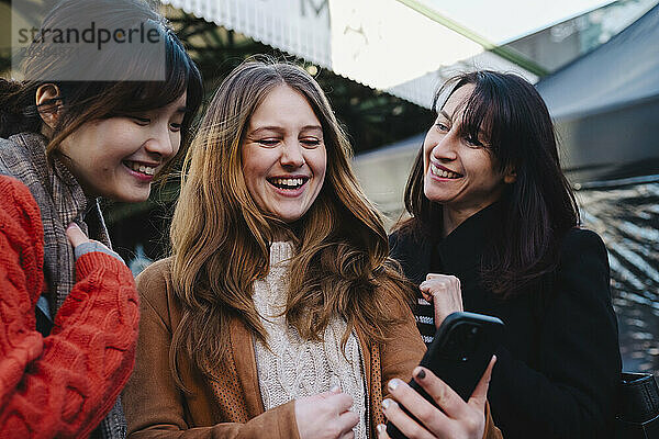 Happy woman showing smart phone to sister and friend