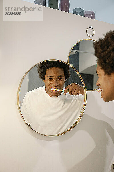 Man brushing teeth looking at reflection on mirror in bathroom