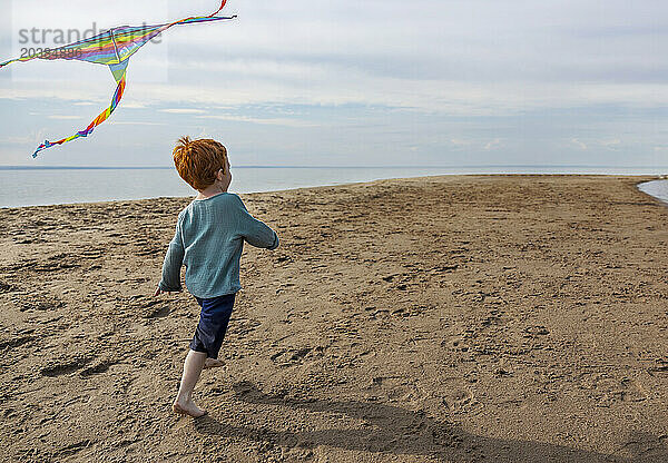 Redhead boy running next to multi colored kite at beach