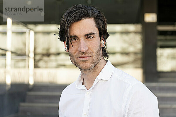 Confident young businessman wearing wireless in-ear headphones