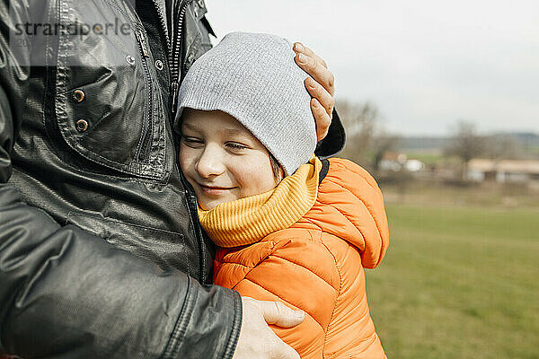 Smiling boy embracing father on sunny day