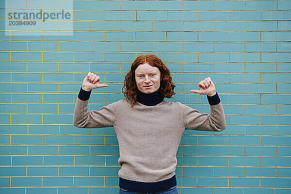 Smiling redhead man gesturing in front of tile wall