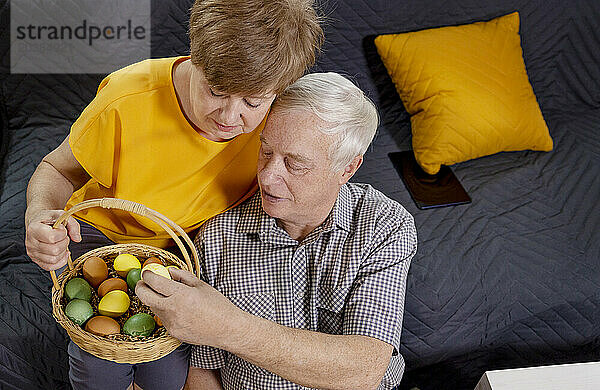 Senior couple examining Easter eggs in basket at home