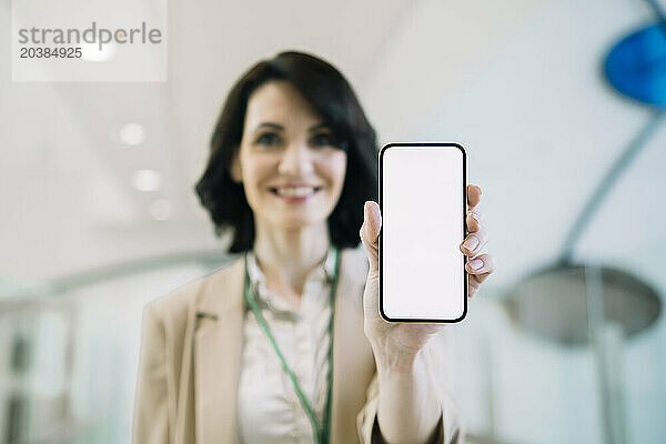 Smiling businesswoman showing smart phone with blank screen at office