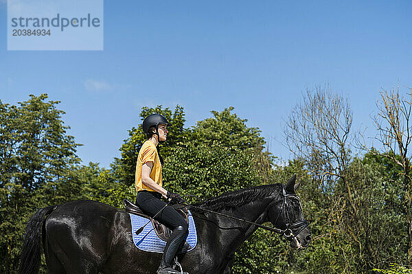 Instructor riding black horse at ranch on sunny day