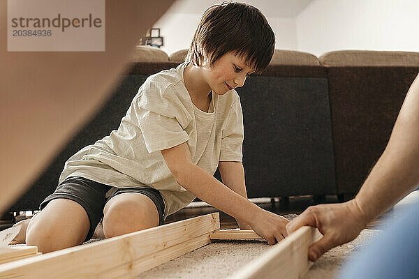 Boy helping father in assembling wooden furniture together at home