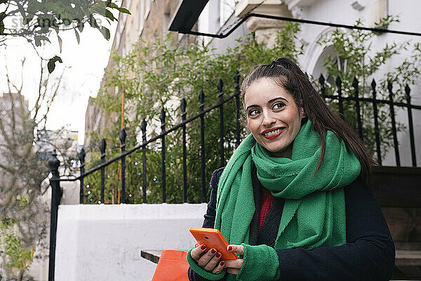 Smiling woman with smart phone near building