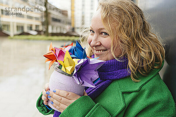 Smiling mature woman holding colorful origami flowers