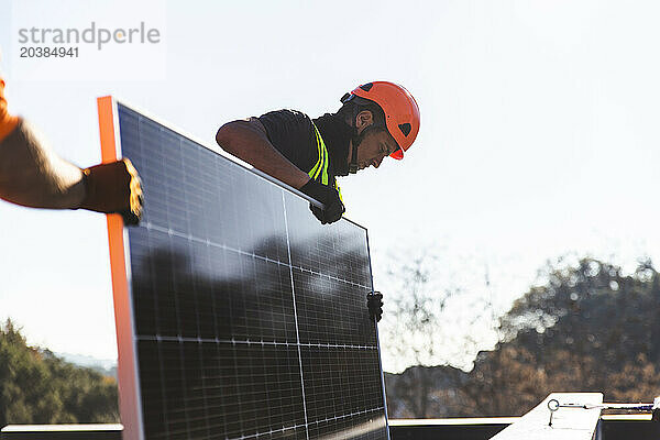 Two workers installing solar panel on sunny day