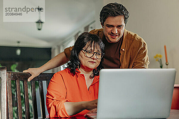 Man helping mother to use laptop at home