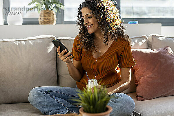 Smiling woman using smart phone on sofa at home