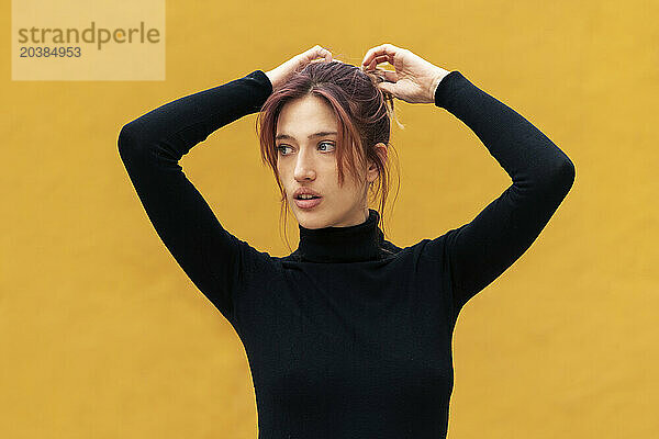 Beautiful young woman with hand in hair against yellow background