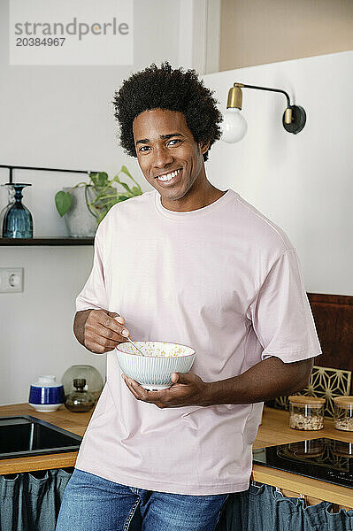 Smiling man eating breakfast standing in kitchen at home