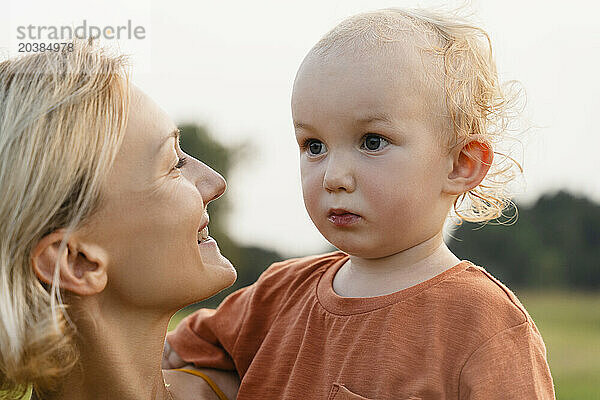 Thoughtful boy with smiling mother in meadow