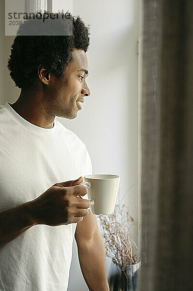 Man with coffee cup looking out of window at home
