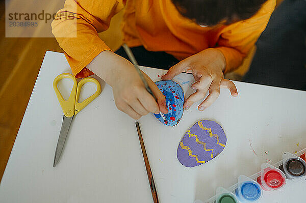 Boy painting cardboard Easter eggs at home