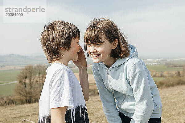 Brother sharing secret with sister at sunny day