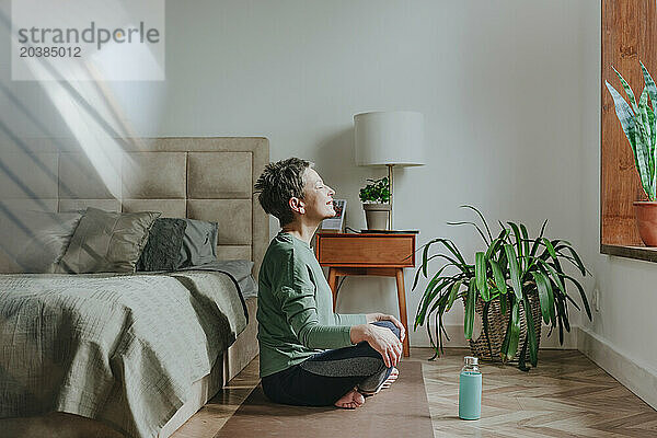Woman meditating near bed at home