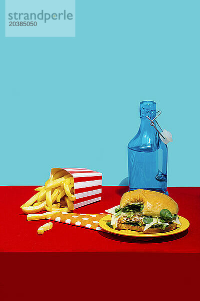 Chicken burger with french fries and soda bottle on table against blue background