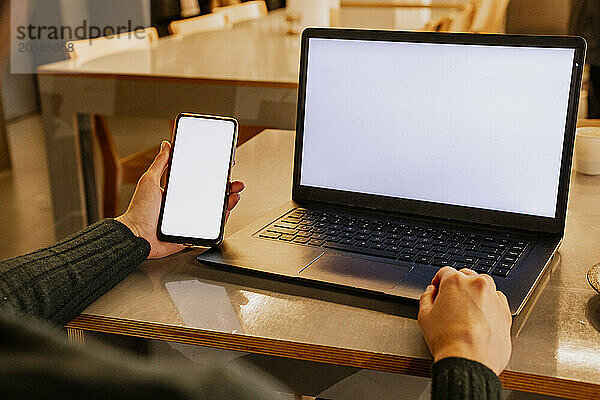 Hand of businesswoman holding smart phone near laptop in office