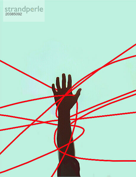 Hand of unrecognizable person tangled in red strings against colored background