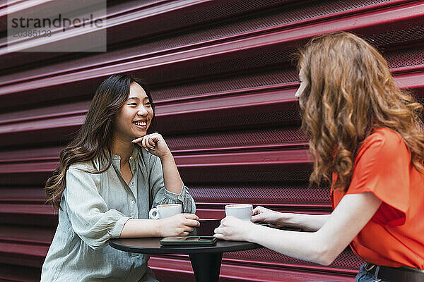 Happy multiracial friends talking near shutter at sidewalk cafe