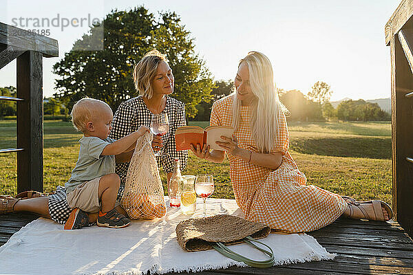 Women reading book sitting by toddler in park