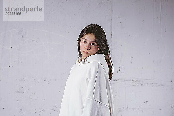 Confident girl in white hoodie posing in front of gray cement background