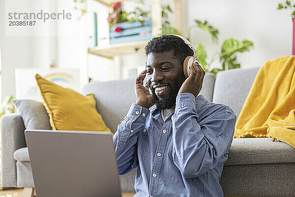 Smiling non-binary person wearing wireless headphones and using laptop at home