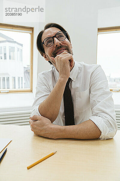 Smiling thoughtful businessman sitting at desk in office