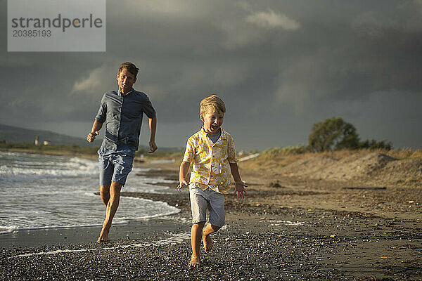 Father and son running on shore at beach