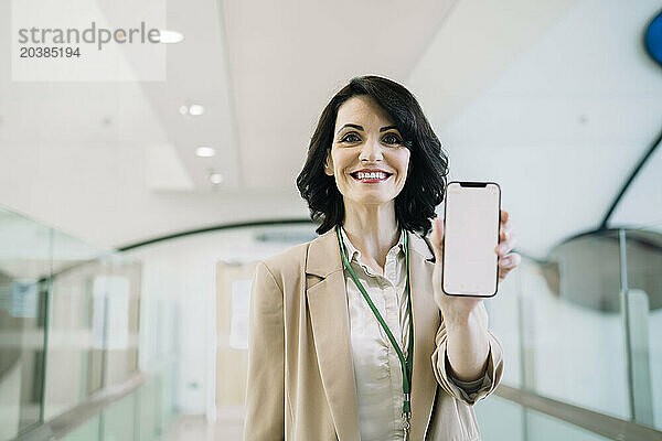 Smiling mature businesswoman showing smart phone with blank screen at office