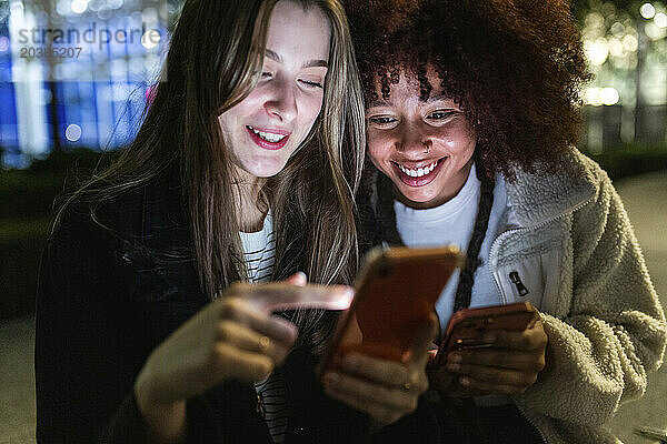 Smiling young women using smart phones at night