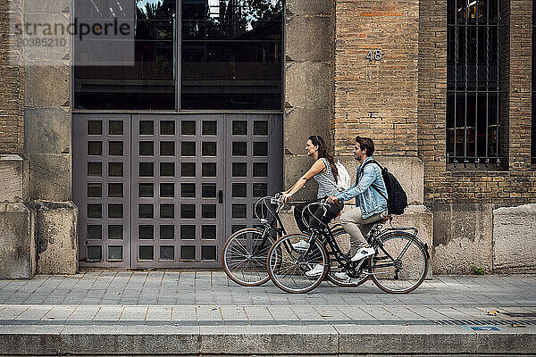 Couple cycling near building entrance on sidewalk