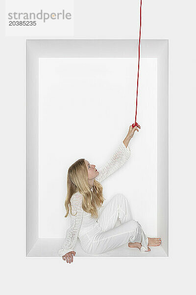 Teenage girl holding thread sitting in alcove against white background