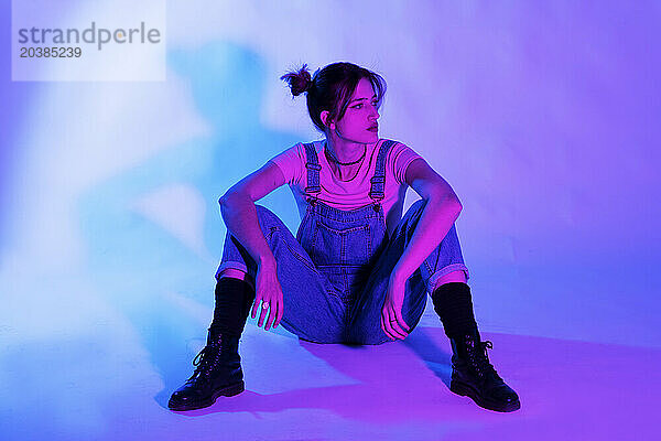 Young woman sitting against illuminated colored background