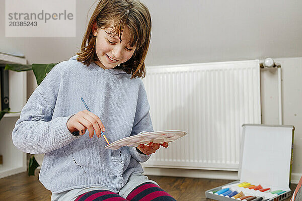 Smiling girl mixing paint on palette at home