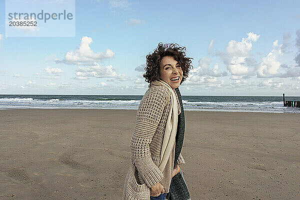 Cheerful woman in cardigan sweater standing at beach