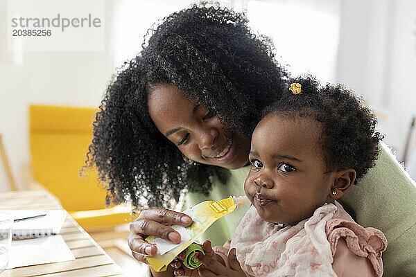 Smiling mother feeding daughter with package food at home