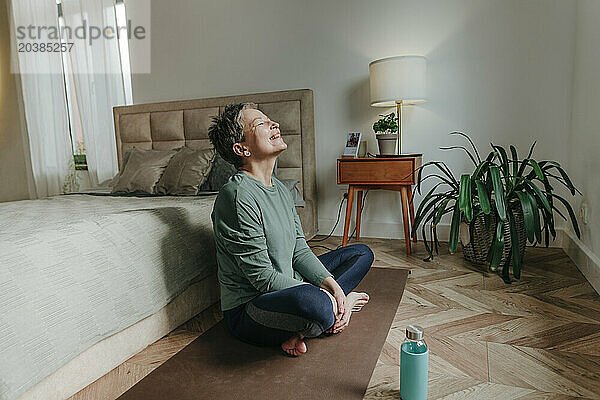 Happy woman sitting with cross-legged near bed at home