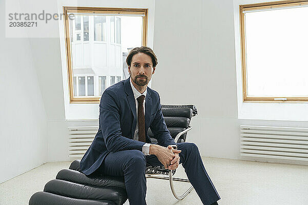 Confident businessman sitting on lounge chair at office