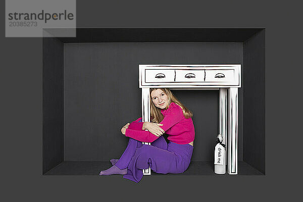 Teenager sitting below table in alcove over black background