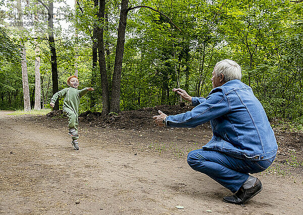 Playful boy running towards grandfather in forest